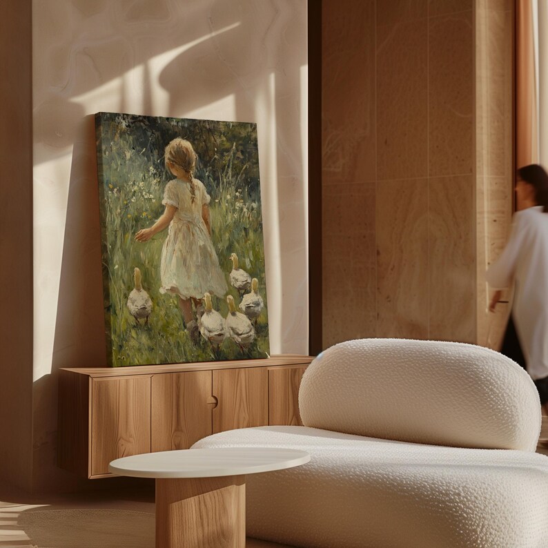 May include: A painting depicting a young girl in a white dress walking through a field with a group of ducks. The painting is framed and hanging on a wall in a room with a light brown wooden cabinet and a white sofa.