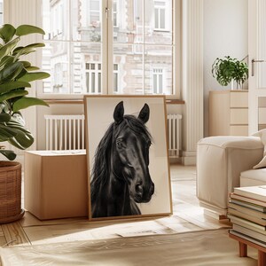 May include: A framed art print featuring a detailed black and white portrait of a horse's head. The artwork is displayed in a light-colored wooden frame, leaning against a neutral-toned wall. The horse's dark mane and features are sharply contrasted.
