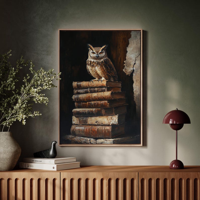 Op de afbeelding: Een ingelijst kunstwerk toont een gedetailleerde uil die bovenop een stapel oude boeken zit. De uil heeft bruine en beige veren, met een gerichte blik. De boeken zijn gebonden in versleten leer, met een donkere achtergrond.