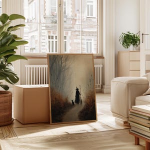 May include: A framed art print depicts a witch with a cat walking down a path in a misty forest. The artwork features muted tones of brown, beige, and gray, creating a mysterious and atmospheric scene. The print is displayed in a light brown wooden frame.