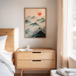 Op de afbeelding: Een houten nachtkastje met twee laden, een witte keramische mok en een boek erop. Het nachtkastje staat naast een bed met witte beddengoed en een houten hoofdeinde. Een ingelijst afdruk van een berglandschap met een rode zon hangt aan de muur achter het nachtkastje.