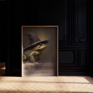 Può includere: Stampa incorniciata con un'illustrazione dettagliata di una rana verde con un cappello da strega nero. La rana è posizionata su una superficie di pietra, con uno sfondo nebbioso. L'opera d'arte è ambientata in un interno scuro ed elegante.