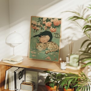 May include: A framed art print depicts a woman and a cat in a tender embrace. The artwork features a soft color palette with floral elements and a vintage aesthetic. The print is displayed on a wooden shelf with books and decorative items.