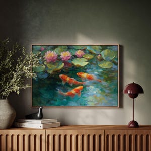 May include: A framed painting depicts koi fish swimming in a pond with lily pads and pink lotus flowers. The artwork has a natural wood frame and is displayed on a wooden cabinet. A burgundy lamp sits on the cabinet.