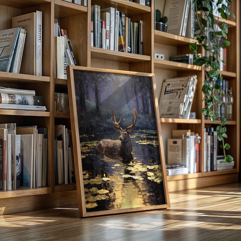 May include: A framed art print featuring a deer in a serene forest setting. The artwork depicts a deer standing in water, surrounded by lily pads, with a forest backdrop. The frame is made of light-colored wood.