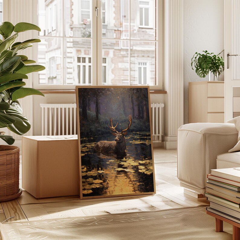 May include: A framed art print depicts a majestic deer standing in a pond, surrounded by lily pads. The artwork features a forest backdrop with a warm, golden light reflecting on the water. The print is displayed in a light-colored wooden frame.