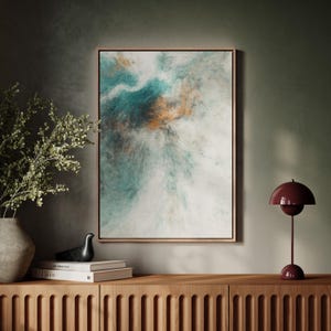 Pu&ograve; includere: Stampa artistica astratta in una cornice di legno. L'opera presenta una miscela di tonalit&agrave; turchese, bianche e arancioni, creando un effetto strutturato simile a una nuvola. L'arte incorniciata &egrave; appesa sopra un mobile in legno, con una lampada decorativa e un vaso.
