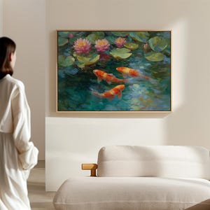 May include: A framed painting depicts a serene pond scene. Pink water lilies bloom among green lily pads. Three orange and white koi fish swim in the turquoise water. The artwork is displayed on a neutral-colored wall.