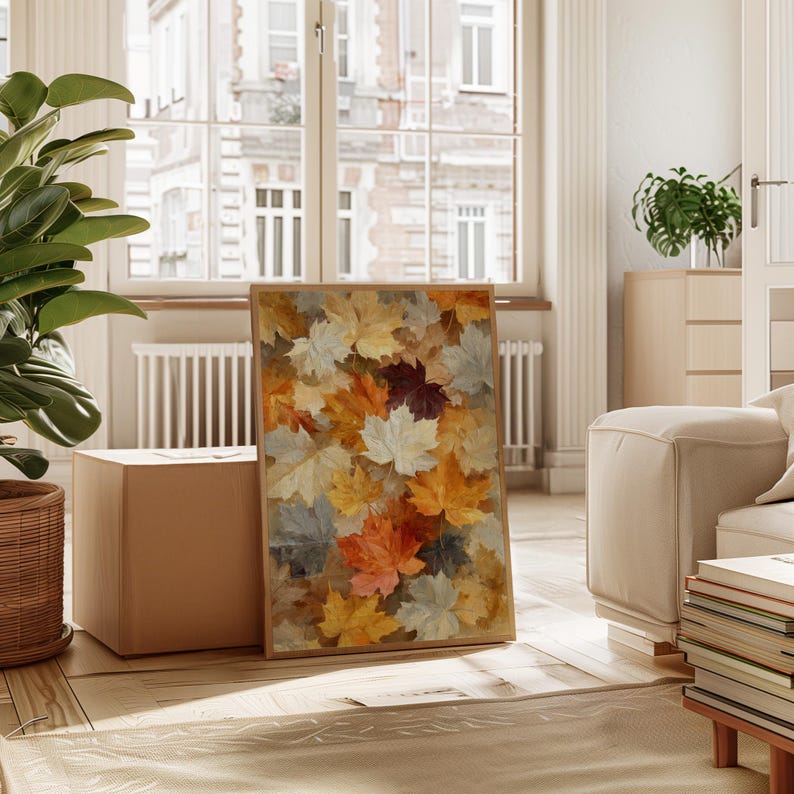 May include: A framed print displaying a collage of autumn leaves in shades of yellow, orange, red, and grey. The artwork is displayed in a bright room with a large window and a neutral colour palette.