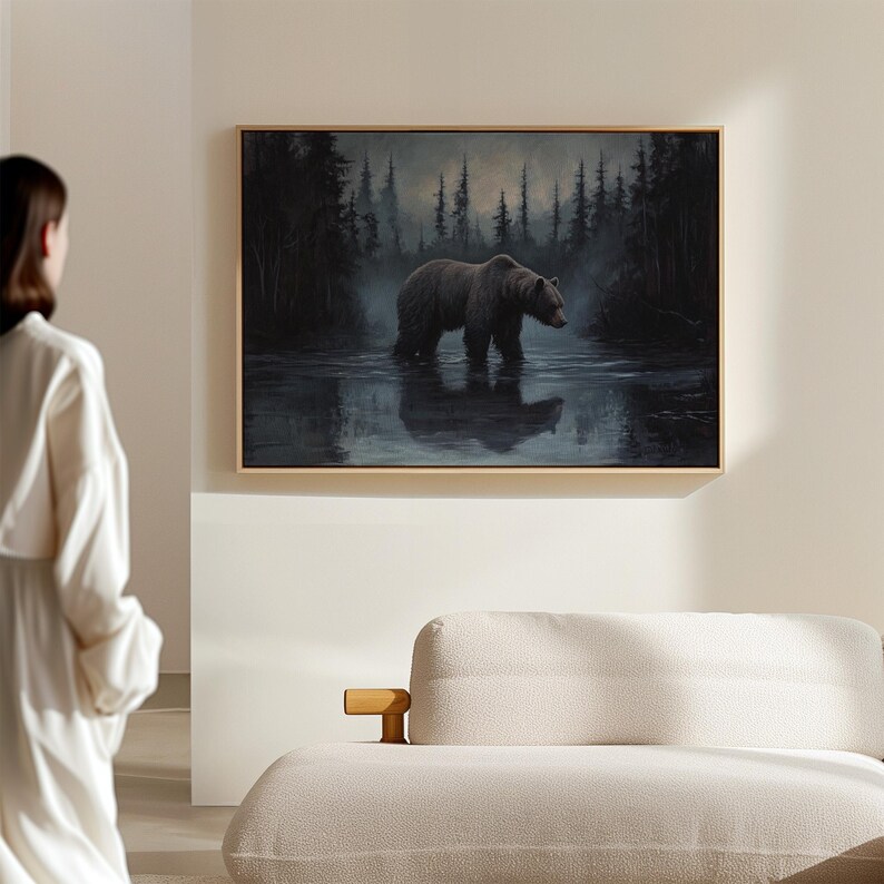 Op de afbeelding: Een ingelijst schilderij toont een bruine beer die door een donker, reflecterend water loopt. De beer staat centraal, met een bos van hoge, donkere bomen op de achtergrond. Het schilderij heeft een gedempte kleurenpalet, met tinten bruin, grijs en zwart.