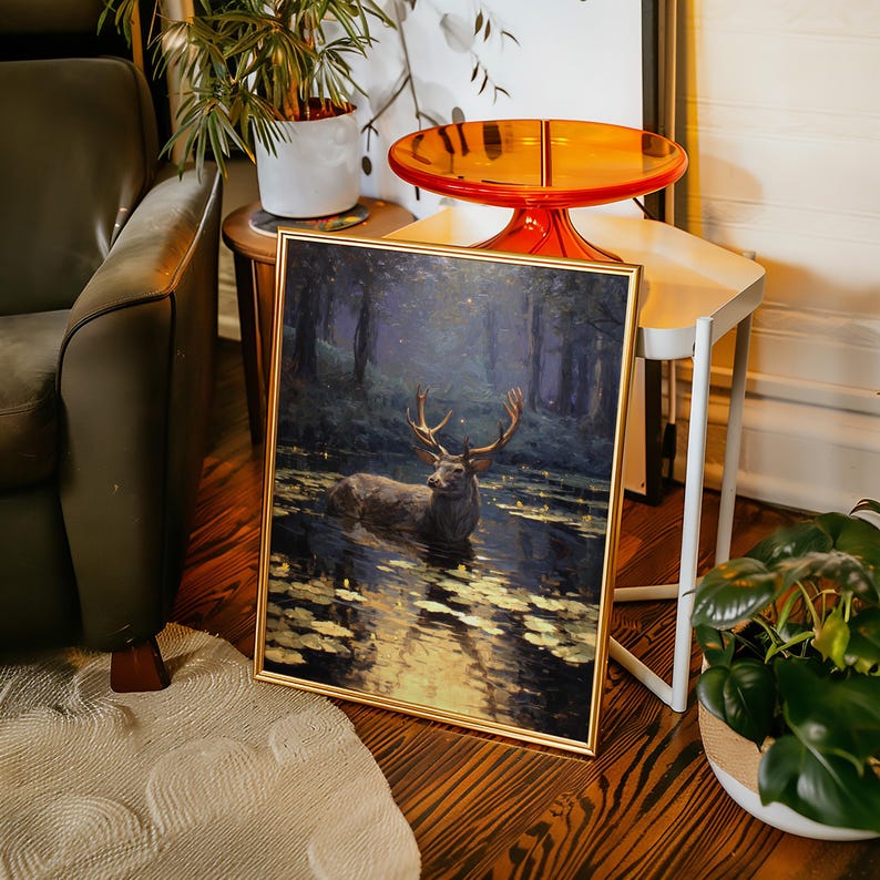 May include: A framed art print depicts a majestic deer standing in a body of water, surrounded by a forest. The artwork features a gold frame and a serene, naturalistic scene with a focus on the animal and its environment.