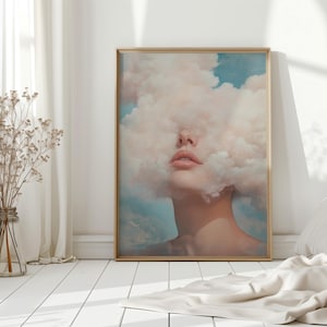 May include: A framed art print showing a surreal portrait. The image features a person's face partially hidden by a cloud of soft, pastel-coloured vapor. The background has hints of blue sky. The frame is a warm gold colour.