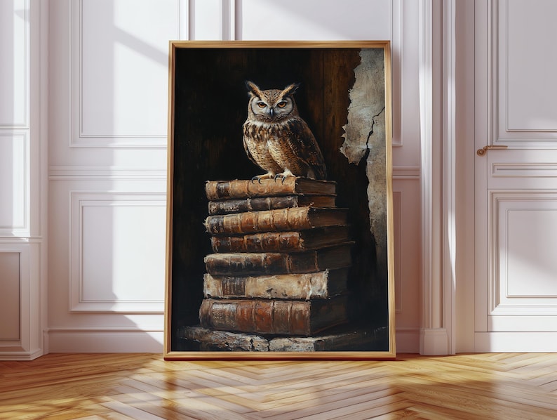 Op de afbeelding: Een ingelijste kunstdruk met een gedetailleerde schildering van een bruine uil die bovenop een stapel oude, ledergebonden boeken zit. De uil heeft grote, expressieve ogen en staat tegen een donkere, getextureerde achtergrond. De lijst is licht van kleur.