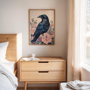 May include: A framed art print featuring a dark blue raven perched amidst pink and peach peonies and other flowers. The artwork has a light wood frame and is displayed on a light-colored wall. The print adds a touch of nature-inspired art to any room.