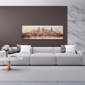 Op de afbeelding: Een witte bank met grijze kussens staat in een moderne woonkamer met een aquarel van een skyline boven een open haard. De kamer heeft een wit tapijt, twee bijzettafels met lampen en een salontafel met een vaas met witte bloemen.