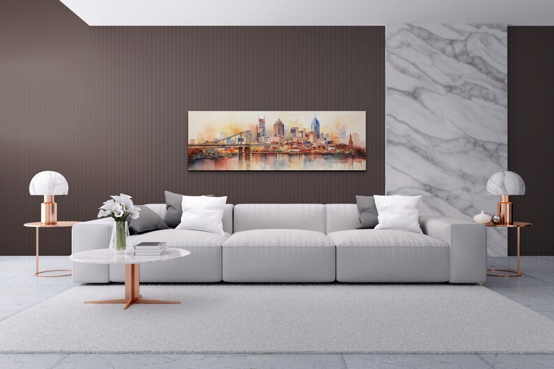 Op de afbeelding: Een witte bank met grijze kussens staat in een moderne woonkamer met een aquarel van een skyline boven een open haard. De kamer heeft een wit tapijt, twee bijzettafels met lampen en een salontafel met een vaas met witte bloemen.