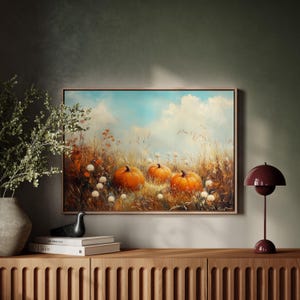 May include: A painting depicting three orange pumpkins in a field with tall grass and white flowers. The sky is blue with white clouds.