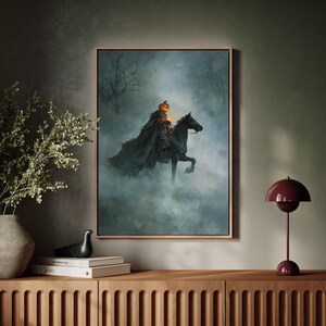 Puede incluir: Una obra de arte enmarcada que representa al Jinete sin Cabeza montado en un caballo negro a través de un bosque brumoso. El jinete tiene una cabeza de calabaza brillante y lleva una capa oscura. La obra está enmarcada en un marco marrón claro, ideal para Halloween.