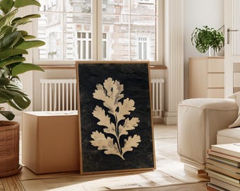 Può includere: Una stampa botanica incorniciata con un design dettagliato di foglie chiare su uno sfondo scuro. L'opera d'arte è esposta su un pavimento in legno in una stanza luminosa, con una grande finestra e uno scorcio di un edificio sullo sfondo. La cornice è di colore marrone caldo.
