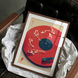 Puede incluir: Impresi&oacute;n art&iacute;stica enmarcada con un dise&ntilde;o de vinilo rojo con ilustraciones de peces koi. La obra de arte tiene un marco de madera y un passe-partout blanco. El brazo del tocadiscos es azul. La impresi&oacute;n descansa sobre papel blanco.