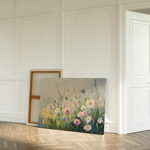 May include: An oil painting on canvas depicts a field of wildflowers in shades of pink, yellow, and blue. The artwork is leaning against a wall in a room with white paneling and a wooden floor. A white door is slightly ajar.