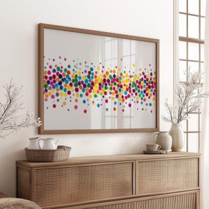 Könnte beinhalten: Ein gerahmter Kunstdruck mit einem farbenfrohen abstrakten Design aus sich überlappenden Punkten in Rosa, Gelb, Blau, Grün und Lila. Das Kunstwerk hängt über einem Holzschrank mit dekorativen Elementen.