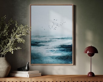 May include: A framed abstract art print depicting a seascape in shades of blue and white, with a flock of birds in flight. The artwork is displayed above a wooden cabinet, alongside a decorative lamp and vase.