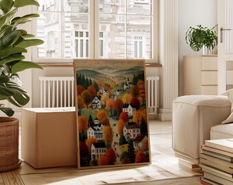May include: A framed print of an autumnal landscape. The artwork features a village surrounded by trees with red, orange, and yellow leaves. White houses and a church are visible, with a path winding through the scene, evoking a sense of warmth.