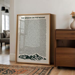 Könnte beinhalten: Gerahmter Druck mit dem Text "THE SERMON ON THE MOUNT" in Schwarz. Der Text befindet sich auf cremefarbenem Hintergrund, mit einer grünen Berglandschaft am unteren Rand. Der Rahmen ist hellholzfarben.