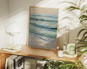 May include: A framed art print depicts an ocean scene with waves and a sandy beach. The artwork is in a light wooden frame and is displayed on a wooden shelf with books, a lamp, and a small radio. The color palette includes shades of blue, green, and beige.