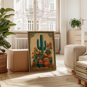 Può includere: Una stampa artistica incorniciata con un cactus turchese e varie piante in vaso con fiori arancioni e rossi. L'opera d'arte ha un'estetica vintage con uno sfondo beige e un bordo decorativo. La stampa è esposta in una stanza luminosa.