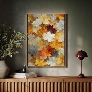 May include: A framed art print depicting a collage of autumn leaves in shades of yellow, orange, white, and burgundy. The artwork is displayed on a wall above a wooden cabinet, with a decorative lamp and vase.