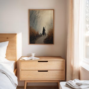 May include: A framed art print depicts a witch walking down a path with a black cat. The artwork is set in a misty forest with muted tones of brown, gray, and beige. The print is displayed above a wooden nightstand.