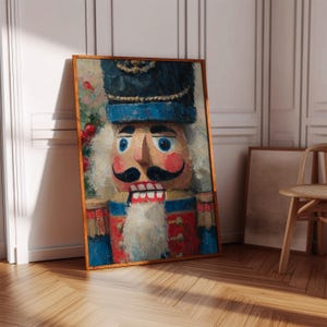 May include: A framed painting of a nutcracker soldier. The artwork features a detailed, colorful depiction of the classic holiday figure, with a blue hat, red and blue uniform, and a white beard. The painting is set against a neutral background.