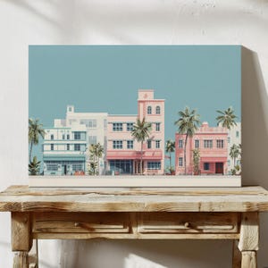 Puede incluir: Una impresión en lienzo rectangular que presenta una fila de edificios de colores pastel con palmeras contra un cielo azul claro. Los edificios son en tonos de rosa, blanco y verde azulado, evocando un tema tropical o costero.