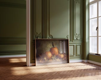 May include: A framed still life painting featuring three orange pumpkins with green stems and autumn leaves. The painting is leaning against a green wall in a room with a wooden floor and a window.