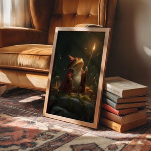 May include: A framed print featuring a whimsical illustration of a frog dressed as a wizard, holding a glowing wand. The frog is wearing a red robe and hat, set against a dark, forest-like background. The frame is a light brown color. The print is leaning against a stack of books.