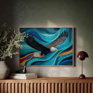 May include: A framed artwork depicts a soaring bald eagle against a backdrop of blue and turquoise waves. The eagle, with its white head, brown wings, and yellow beak, is the focal point. The artwork is displayed on a wooden cabinet.