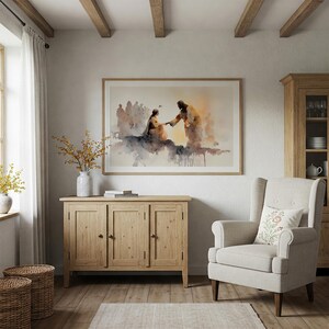 May include: A watercolor painting in a light wood frame hangs above a wooden cabinet. The painting depicts two figures in warm tones, with a crowd in the background. A beige armchair with a floral pillow sits nearby.