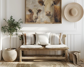 May include: A rustic living room scene featuring a framed cow painting, a wooden bench with pillows, and a woven rug. The painting depicts two cows in shades of brown and cream. A large sun hat hangs on the wall.