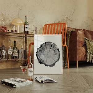 May include: A framed black and white print of a tree cross-section. The print is displayed in a room with a bar cart, orange chair, and leather sofa. A bottle of wine and a martini glass are in the foreground.