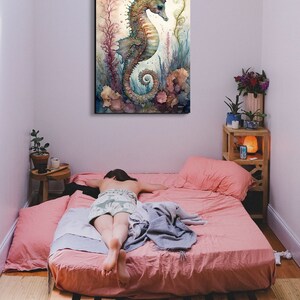 Puede incluir: Una pintura de acuarela de un caballito de mar con una corona de coral y algas marinas. El caballito de mar es azul, verde y marr&oacute;n sobre un fondo amarillo. La pintura est&aacute; enmarcada y colgada en una pared sobre una cama.