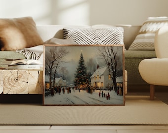 May include: A framed winter landscape painting depicts a snowy village scene with a decorated Christmas tree. People are gathered on a snow-covered street, with houses and trees in the background. The artwork is in a wooden frame.