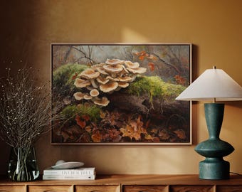 May include: A framed painting depicts a cluster of mushrooms on a moss-covered log in a forest setting. The artwork features a palette of earthy tones, including browns, greens, and oranges. A teal lamp with a white lampshade sits on a wooden cabinet.