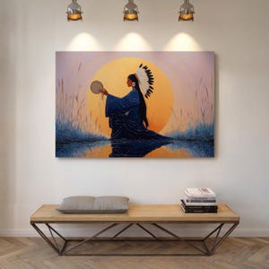 May include: A canvas print shows a Native American figure in a blue robe holding a drum, set against a sunset backdrop. The artwork features a vibrant orange sun, with reflections in the water below. The figure wears a traditional headdress.
