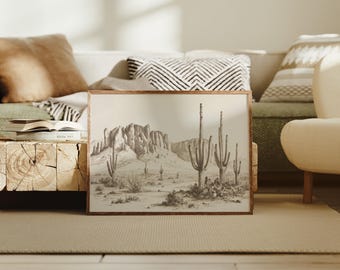 May include: A framed sepia-toned print of a desert landscape featuring cacti and a mountain range. The artwork is displayed in a wooden frame and rests on a beige rug. The print depicts a serene desert scene.