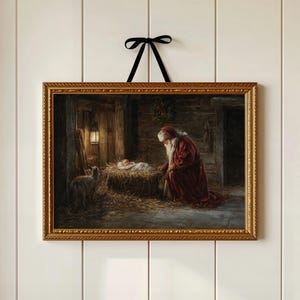 Puede incluir: Una pintura navideña enmarcada que representa una escena de la Natividad con Papá Noel arrodillado ante el niño Jesús en un pesebre. La pintura tiene un marco dorado adornado y está suspendida por una cinta negra contra una pared blanca.