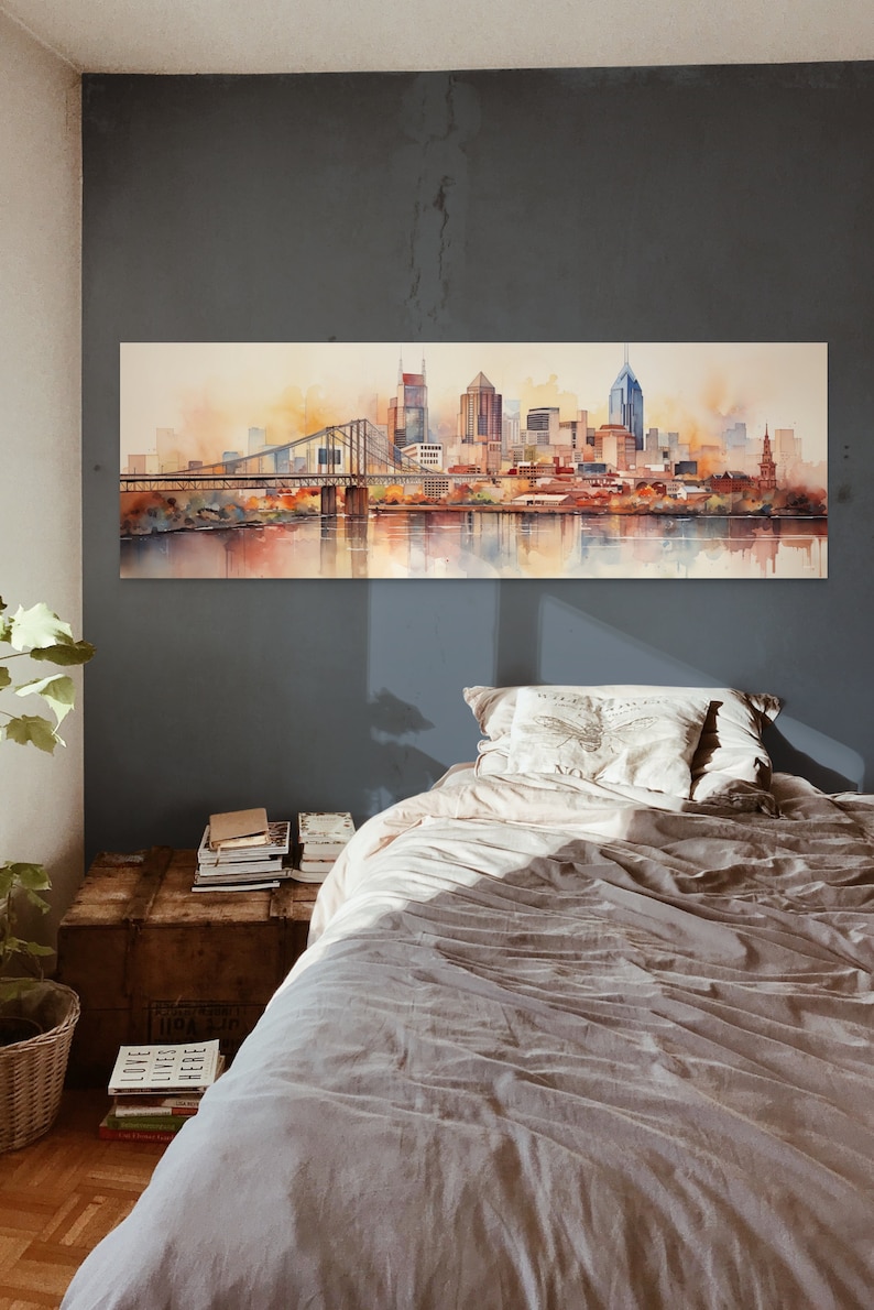 Op de afbeelding: Een aquarel schilderij van een skyline met een brug op de voorgrond. De stad is afgebeeld in tinten bruin, oranje en geel, met een rivier op de voorgrond. Het schilderij is ingelijst en hangt aan een muur boven een bed.
