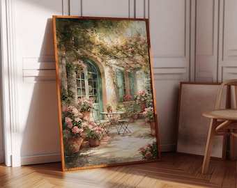 Può includere: Una stampa ad acquerello incorniciata raffigura una scena all'aperto affascinante. Un tavolino e sedie sono su un patio in pietra, circondati da fiori rosa in vaso e vegetazione lussureggiante. L'edificio presenta una porta e persiane verdi, creando un'atmosfera serena e invitante.