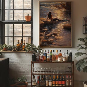 May include: A framed painting of a mermaid sitting on rocks near the water. A bar cart with various bottles of liquor and glassware is in the foreground. The room has a large window with plants on the windowsill.